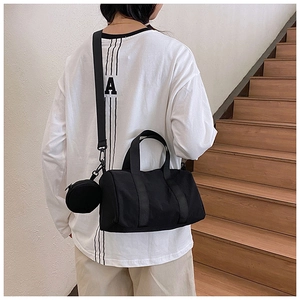Detalle de bolso Boston negro con correa ajustable y monedero pequeño usado por una modelo
