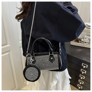 Detalle de bolso cilíndrico negro con tachuelas, cadena y colgante redondo a juego