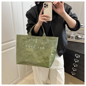 Dettaglio del tessuto testurizzato verde e della stampa bianca TOTE BAG sulla borsa