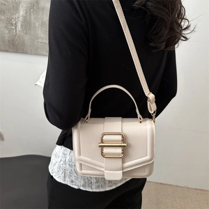 Petit sac à main beige minimaliste avec boucle dorée porté par un mannequin élégant
