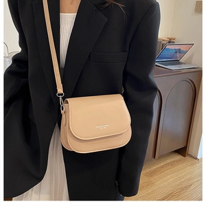 Gros plan sur un sac besace beige avec imprimé mode porté sur un blazer noir