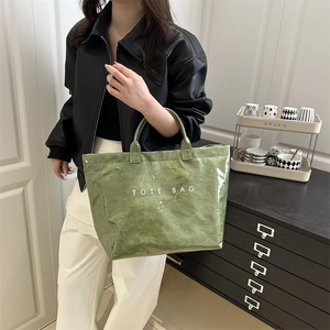 Borsa tote verde testurizzata con stampa bianca indossata da una modella in casa moderna
