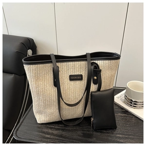 Detail of herringbone straw tote bag with black leather trim and metal logo plaque