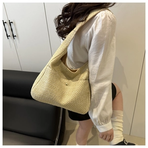 Détail d'un sac cabas en paille tressée avec poche latérale et bouton doré décoratif