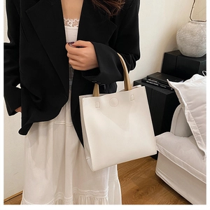Close-up of a white tote bag with beige handles on a sofa in a minimalist setting