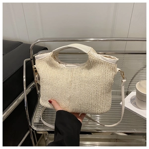 Détail d'un sac cabas en paille tissée avec anses en cuir crème et ferrures dorées