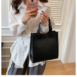 Sac fourre-tout noir minimaliste en cuir lisse porté par un mannequin pour le quotidien