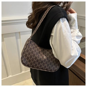 Close-up of retro brown crescent bag with M-letter pattern on a female model shoulder