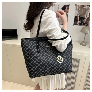 Detalle de bolso tote negro con patrón de cadena y colgante dorado en oficina