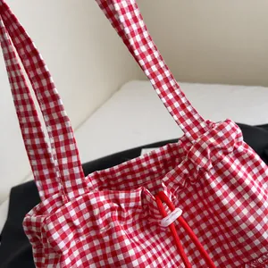 Detail of red and white gingham tote bag featuring long shoulder straps and drawstring closure