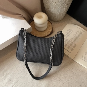 Minimalist black woven underarm bag with silver chain detail and herringbone texture