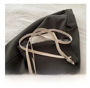 Détail d'un sac demi-lune crème avec bandoulière réglable posé sur un tissu marron foncé