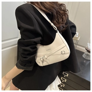 Détail du sac demi-lune crème avec lanières croisées et boucles argentées sur un blazer noir