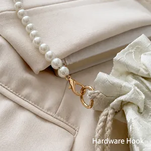 Detail of white faux pearl strap with golden hardware and textured drawstring pouch