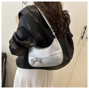 Sac hobo argenté avec détail nœud porté par un mannequin en veste de cuir