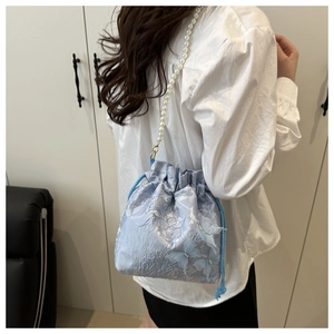 Detail of light blue bucket bag with 3D butterflies and elegant pearl strap on model