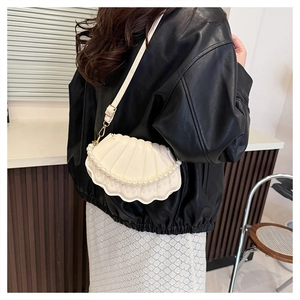 Detail of shell-shaped white bag with pearl handle worn by model in black leather jacket