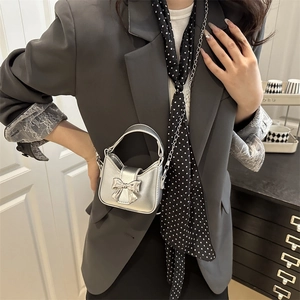 Silver mini square handbag with bow lock and chain strap carried by a model