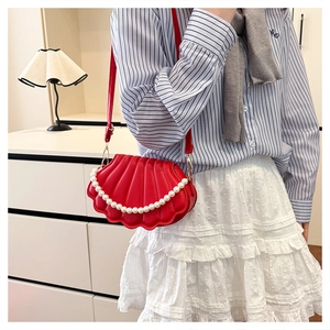 Detail of red shell-shaped handbag with large white pearl trim and golden hardware