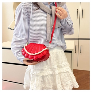 Macro shot of red shell-shaped crossbody bag with texture and pearl handle detail