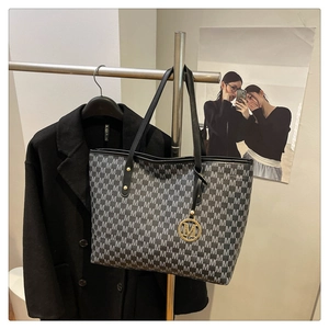 Detailed view of tote bag with M-pattern print and gold charm styled with black blazer