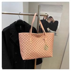 Detail of large pink tote bag with brown letter patterns and golden metal logo pendant