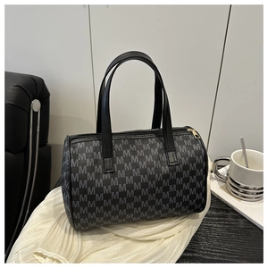Détail du sac à main cylindrique à motif M avec anses en cuir sur un bureau minimaliste