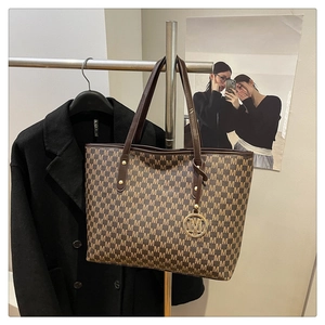 Detail of classic M-print tote bag with dark brown leather handles and gold metal charm