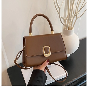 Detailed view of brown leather handbag with gold oval clasp and adjustable shoulder strap