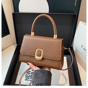 Detail of a brown leather handbag featuring a golden textured buckle and fixed top handle