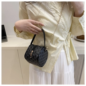 Détail d'un sac cylindrique noir avec monogramme M gris et chaîne en métal doré