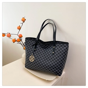 Detail of a large black tote bag with grey monogram pattern and golden M logo charm