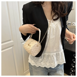 Détail d'un sac cylindre beige avec imprimé M et bandoulière chaîne dorée