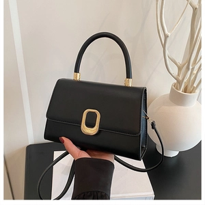 Detailed close-up of a black leather handbag featuring a stylish gold oval clasp
