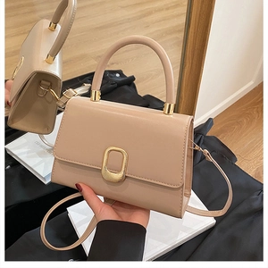 Detail of beige handbag featuring gold metal clasp and detachable shoulder strap