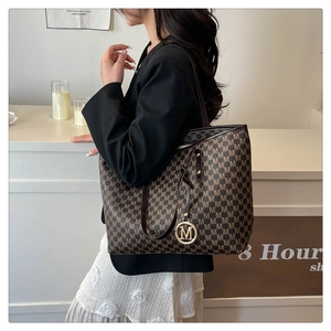 Detail of brown tote bag with M-pattern print and golden logo charm on a female model