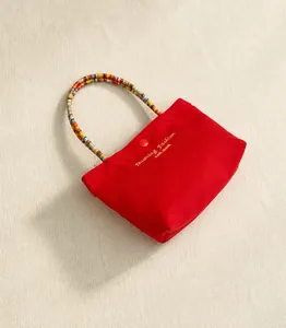 Detail of red canvas handbag with golden lettering and colorful beaded handle with button