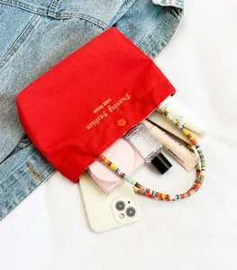 Detail of red canvas tote bag showing interior space with phone, cosmetics and beaded strap