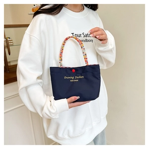 Detail of navy canvas tote bag with multicolor woven handles and golden logo text
