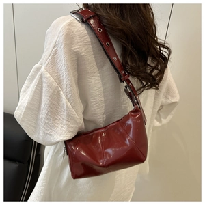 Detail of burgundy patent leather underarm bag with metal eyelets on wide strap