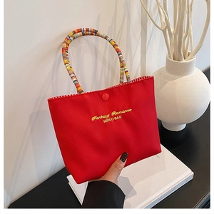 Détail du sac en toile rouge avec broderie dorée et poignée ronde tissée colorée