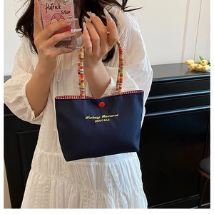 Détail d'un sac bleu foncé avec des poignées en perles colorées et un bouton rouge