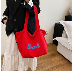 Detailed view of red canvas tote bag with blue Beach text and adjustable drawstring cord