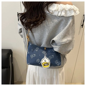 Blaue Denim Schultertasche mit weißen Bärenprints und Cupcake-Anhänger am Modell