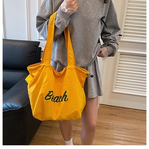 Detail of a yellow canvas tote bag with green Beach lettering and drawstring closure