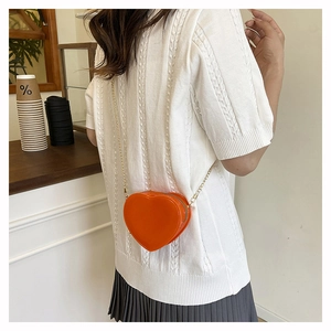 Schicke orangefarbene Mini-Herz-Tasche mit Goldkette getragen zu weißem Strick-Outfit