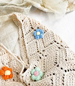 Detail van de handgehaakte beige tas met kleurrijke gebreide bloemen en zachte textuur