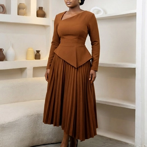 Detail of caramel pleated dress featuring asymmetrical neckline and structured peplum waist