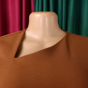Detail of caramel brown dress featuring textured fabric and asymmetrical neckline design