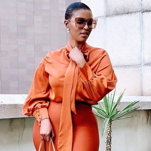 Detail einer eleganten orangefarbenen Satinbluse mit Halsschleife und Faltenmanschetten